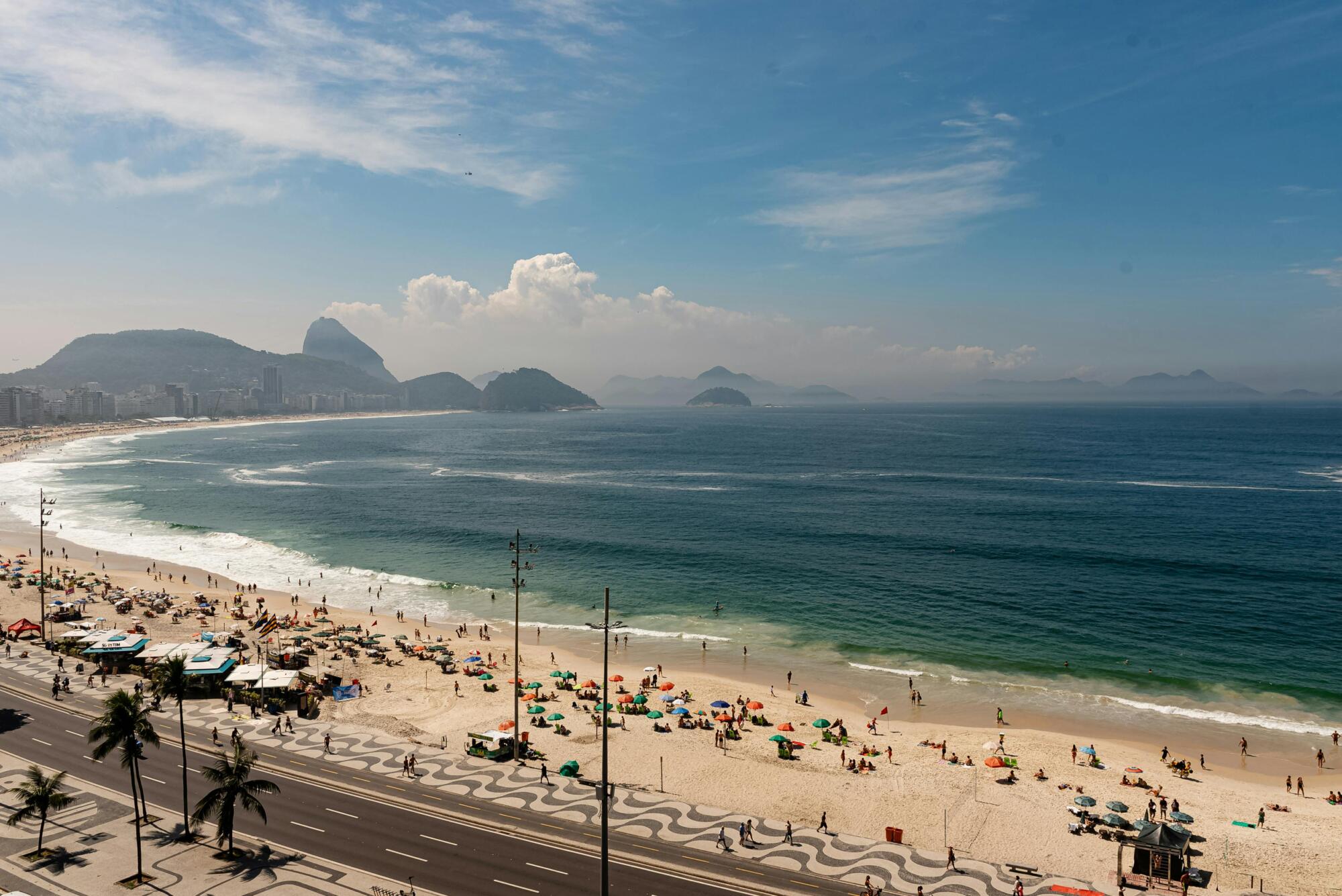Stunning aerial view of Copacabana Beach with bustling activity and iconic Sugarloaf Mountain in Rio de Janeiro.